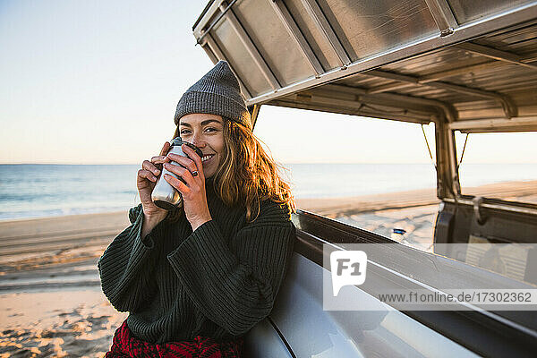 Junge Frau genießt Kaffee im Reisebecher beim Camping am Strand