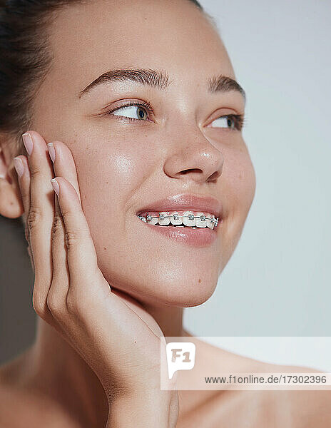Junge schöne Frau mit sauberer frischer Haut mit Zahnspange lächelnd - weißer Hintergrund