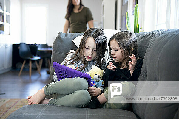 Zwei kleine Mädchen sitzen auf der Couch und benutzen ein Tablet.