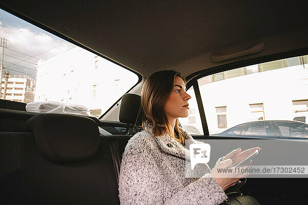 Nachdenkliche Frau  die ihr Smartphone während der Fahrt im Auto hält