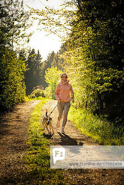 Young woman and dog running together in sunny forest.