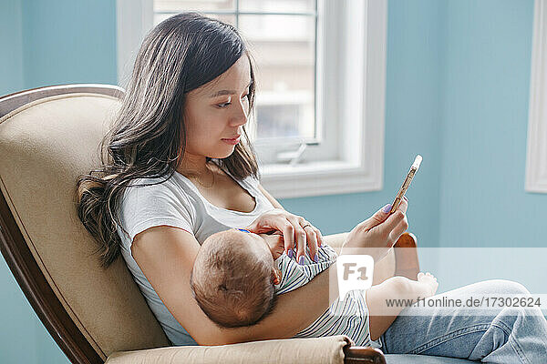 Asiatische Mutter hält ihren neugeborenen Sohn im Arm und kauft Lebensmittel online im Internet.