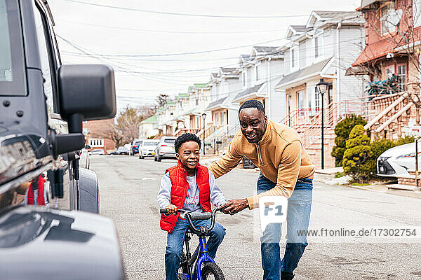 Lächelnder Vater  der seinem Sohn hilft  auf der Straße Fahrrad zu fahren