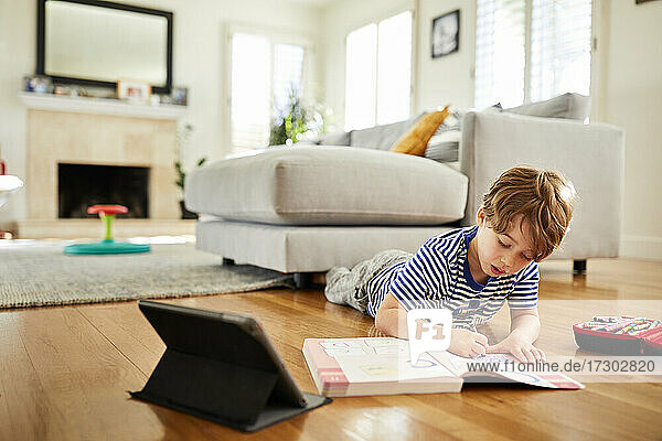 Junge malt mit Buntstift in einem Buch  während er zu Hause e-learning betreibt