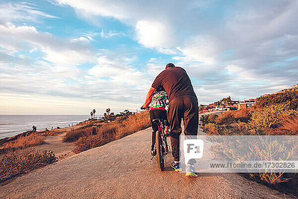 Vater hilft seinem Sohn beim Radfahren auf einem Küstenweg.