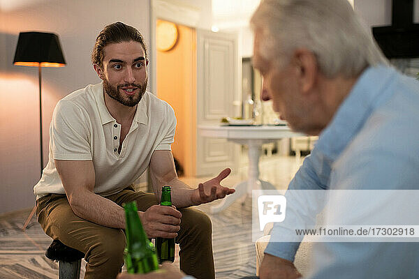 Young man drinking beer and speaking with grandfather