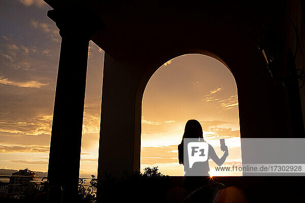 Silhouette einer jungen Frau  die bei Sonnenuntergang ein Selfie macht