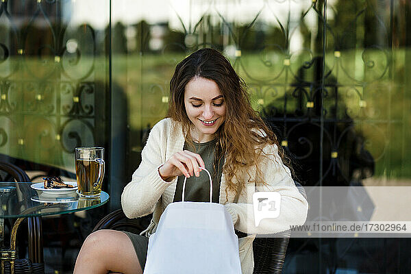Ein Mädchen auf der Straße sitzt an einem Tisch und schaut lächelnd in eine Papiertüte.