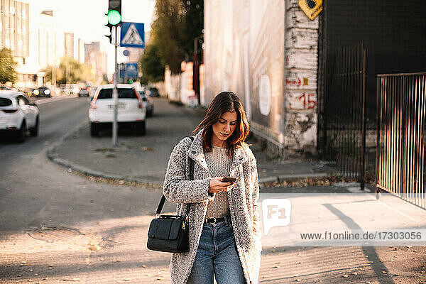 Nicht-binäre Frau benutzt Smartphone beim Spaziergang in der Stadt