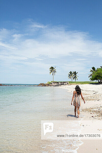 Junge Frau geht im Kleid am Strand entlang
