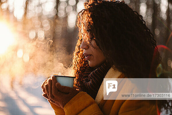 Young woman holding cup of hot tea standing outdoors during winter