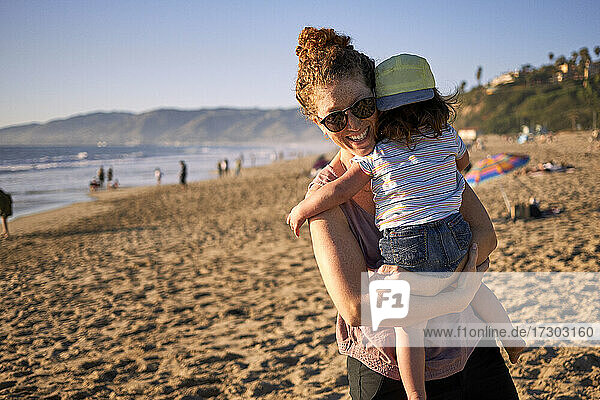 Smiling mother carrying daughter at beach during weekend