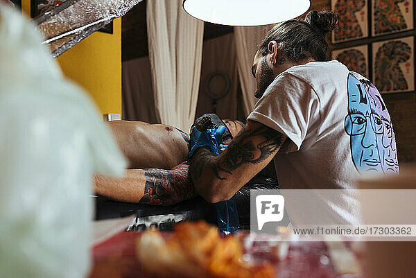 Rückenansicht eines Tätowierers bei der Arbeit am Arm eines Kunden in seinem Studio.