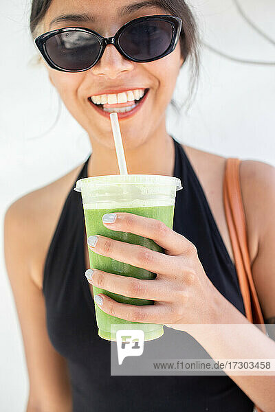 Junge Frau mit Sonnenbrille hält grünen Saft