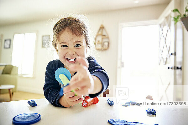 Porträt eines fröhlichen Mädchens  das zu Hause auf dem Tisch mit Spielzeug spielt