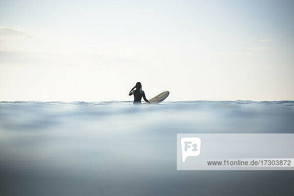 Asian Woman waiting for waves during sunrise summer surf session
