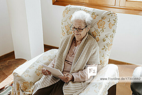 Lächelnde ältere Frau  die auf dem Sofa ein Tablet benutzt