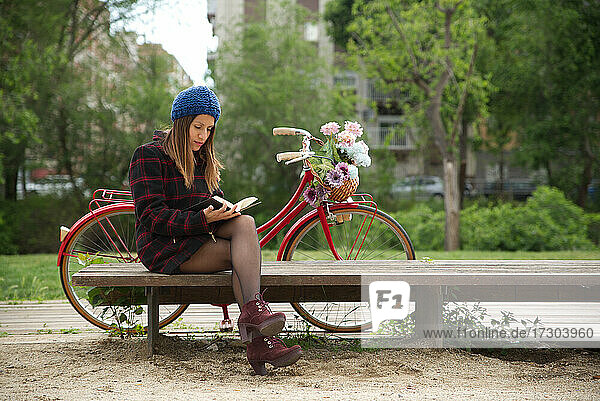 Woman reading a book  a red bicycle and a basket of colorful flowers.
