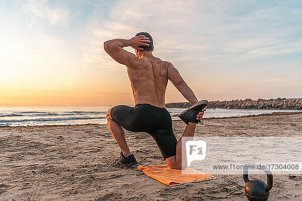 muskulöser Mann beim Training am Strand bei Sonnenaufgang