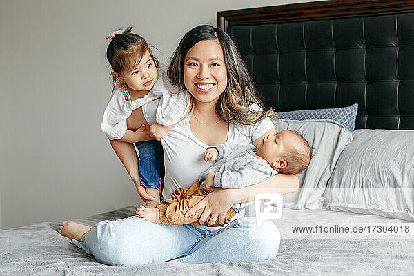 Feiertag Muttertag. Asiatische chinesische glückliche Mutter sitzt spielend auf dem Bett
