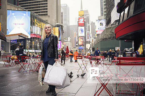 Positive Frau mit Einkaufstüten auf dem verregneten Times Square