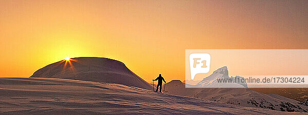 Panoramablick auf einen Forscher auf einem verschneiten Bergkamm bei Sonnenuntergang.