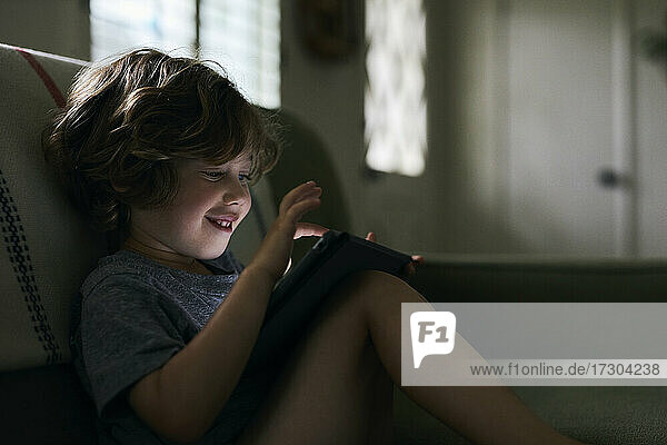 Junge lächelt  während er ein digitales Tablet zu Hause benutzt