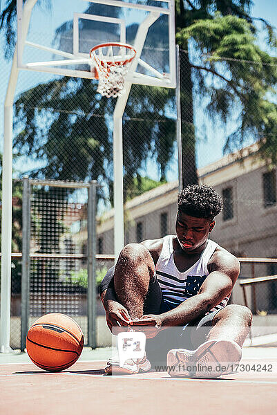 Porträt eines schwarzen afroamerikanischen Jungen  der seine Schnürsenkel auf einem städtischen Basketballplatz bindet.