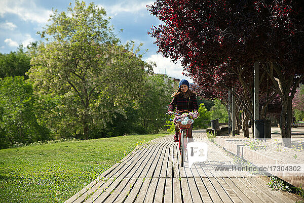 Frau fährt auf einem roten Fahrrad mit einem Korb voller bunter Blumen.