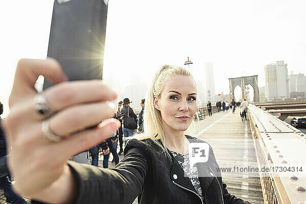 Zufriedene Frau  die ein Selfie auf einer Brücke in einer städtischen Metropole macht