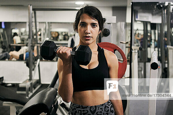 Young woman lifts weights in a gym looking at camera