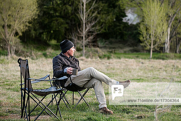 Mann mittleren Alters hält Becher mit Kaffee auf dem Campingplatz