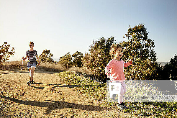 Cheerful girl hiking with mother against clear sky on sunny day