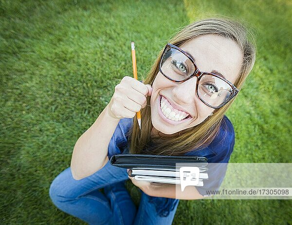 Spaß Weitwinkel Porträt der hübschen jungen Frau mit Bücher und Bleistift sitzen im Gras im Freien