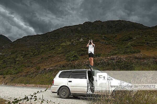Mann mit Kamera auf dem Autodach  Queenstown  Region Otago  Queenstown-Lakes District  Südinsel  Neuseeland  Ozeanien