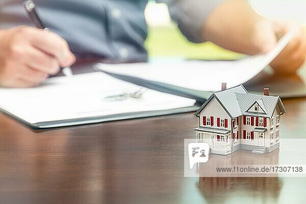 Mann beim Unterschreiben von Immobilienvertragspapieren mit kleinem Modellhaus davor