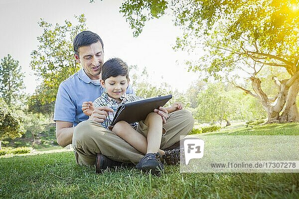 Hübscher gemischtrassiger Vater und Sohn spielen draußen auf einem Computer-Tablet