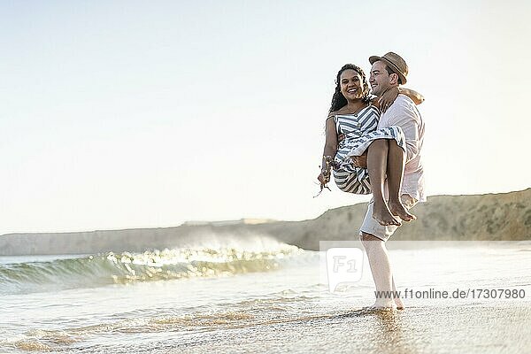 A young man carrying his beloved woman on the beach by sunset in Algarve  Portugal  Europe