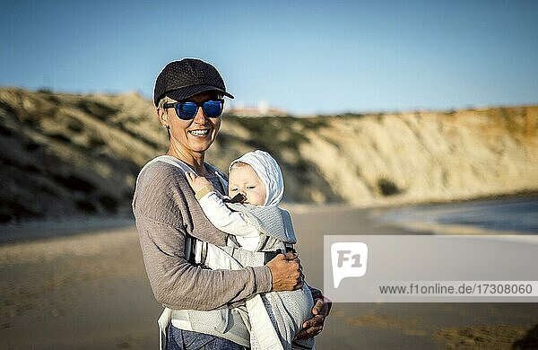 Eine Mutter mit ihrem Sohn in der Trage am Strand in Portugal