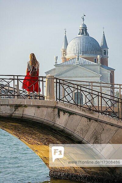 Junge Frau in Rotem Kleid auf einer Brücke an einem Kanal  hinten Kirche Chiesa del Santissimo Redentore  Venedig  Venetien  Italien  Europa