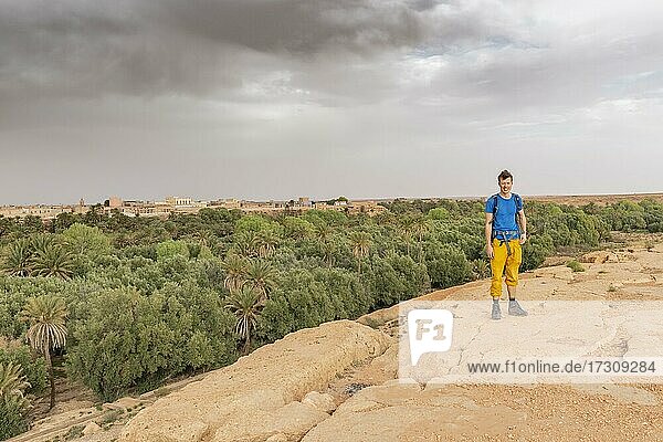 Young man at a cliff edge  behind valley full of palm trees at the oasis Source Bleu  Blue Spring  Madkhal Meski  Morocco  Africa