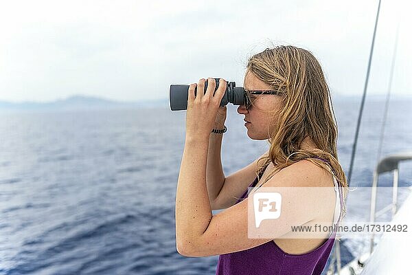 Junge Frau schaut durch ein Fernglas  auf Segelboot  Dodekanes  Griechenland  Europa