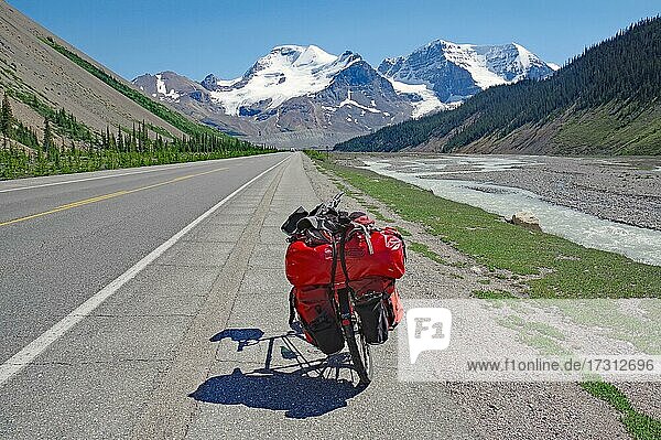Beladenes  rotes Reiserad auf gerader Straße  hohe Berge und Gletscher im Hintergrund  Icefields Parkway  Rocky Mountains  Alberta  Kanada  Nordamerika