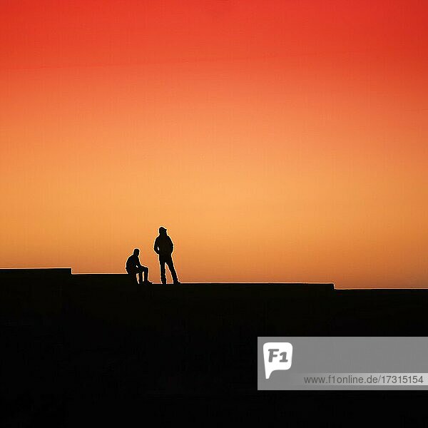 Zwei Mönner schauen in die Ferne  Silhouetten auf einer Mauer bei Sonnenuntergang  Essaouira  Atlantikküste  Marrakesch-Safi  Marokko  Afrika
