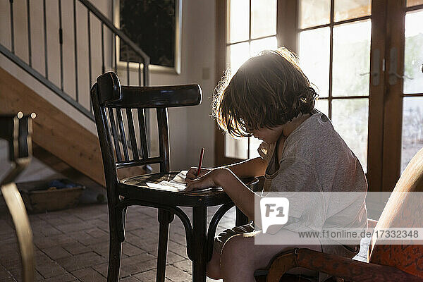 young boy writing on small chair at sunset