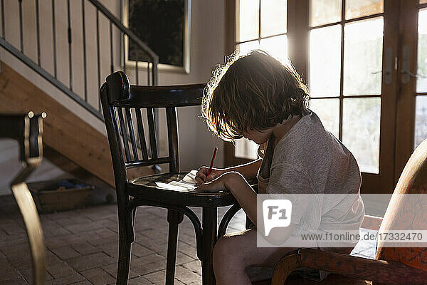 young boy writing on small chair at sunset