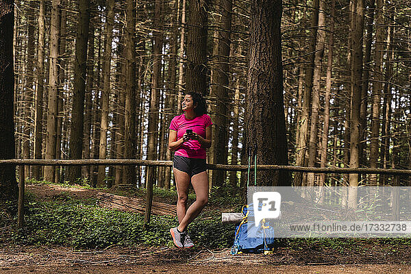Weibliche Wanderin schaut weg  während sie ihr Handy vor den Bäumen im Wald hält
