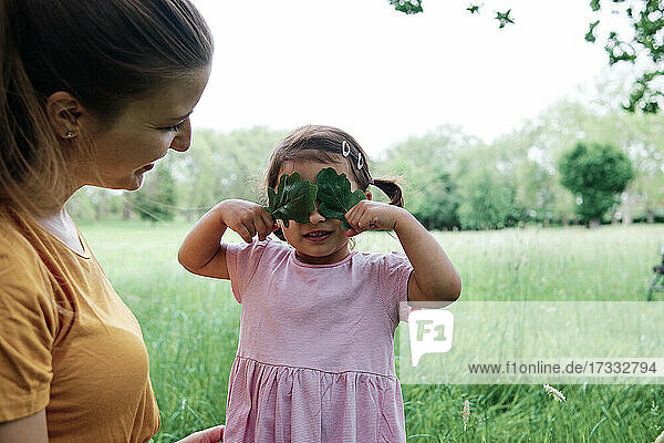 Mother looking at daughter covering eyes with leaves