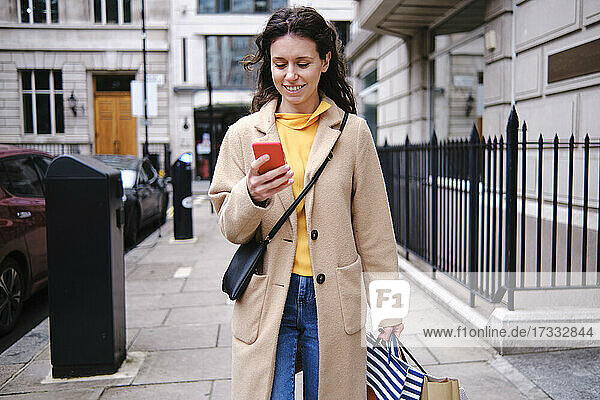 Lächelnde Frau benutzt ihr Smartphone beim Einkaufen in der Stadt