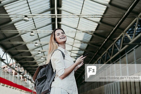 Cheerful young female passenger wearing backpack looking away at railroad station
